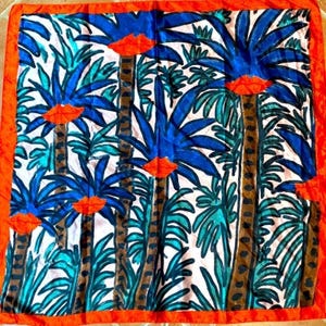 May include: Square silk scarf with a vibrant tropical design. The scarf features blue palm trees, teal foliage, and orange lips against a white background. It has a bright orange border, creating a bold and eye-catching accessory.
