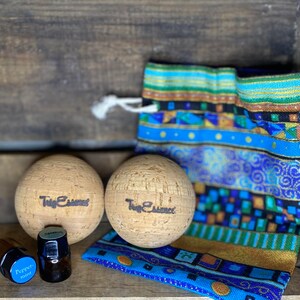 Puede incluir: Dos bolas de masaje de corcho marrón con el texto "Twig Essences" impreso en ellas, una pequeña botella de aceite esencial etiquetada como "Peppermint" y una bolsa de tela con estampado azul y dorado.
