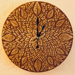 Puede incluir: Un reloj de madera con un diseño marrón intrincado de hojas y una esfera negra con manecillas.