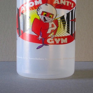 Puede incluir: Una botella de agua de pl&aacute;stico transparente con un logotipo de Atom Ant's Gym rojo, amarillo y negro. El logotipo presenta una hormiga de dibujos animados que lleva un casco y un traje rojo con una gran letra "A" en el pecho.