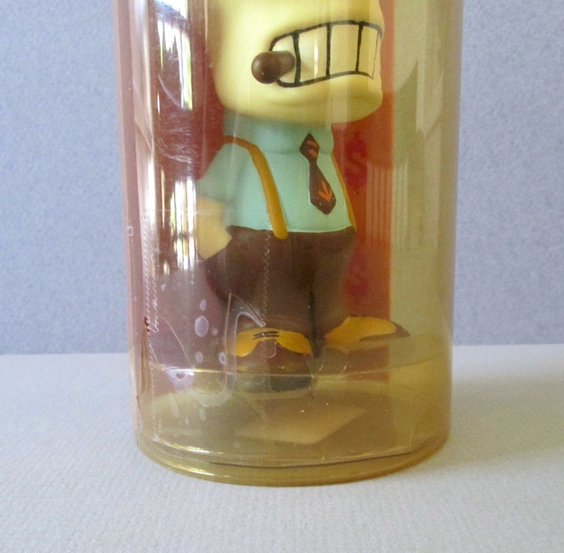 K&ouml;nnte beinhalten: Ein Plastikbeh&auml;lter mit einem durchsichtigen Deckel und einem gelben Boden. Im Inneren des Beh&auml;lters befindet sich eine Comicfigur mit einem braunen Hut, einem blauen Hemd, einer braunen Krawatte und einer braunen Hose. Die Figur h&auml;lt eine braune Zigarre im Mund.
