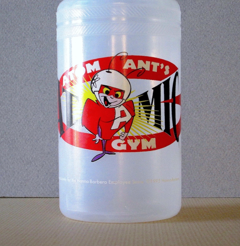 Puede incluir: Una botella de agua de pl&aacute;stico blanca con un logotipo de Atom Ant's Gym rojo, amarillo y negro. El logotipo presenta una hormiga de dibujos animados con un casco y un traje rojo.