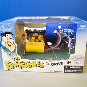May include: A boxed McFarlane Toys set featuring The Flintstones at the Drive-In. The box has images of Fred Flintstone and the drive-in scene. The set includes figurines of the characters and a diorama of the drive-in.