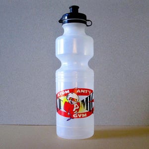 Puede incluir: Una botella de agua de pl&aacute;stico transparente con una tapa negra y una pegatina roja, amarilla y negra que dice "Atom Ant's Gym".