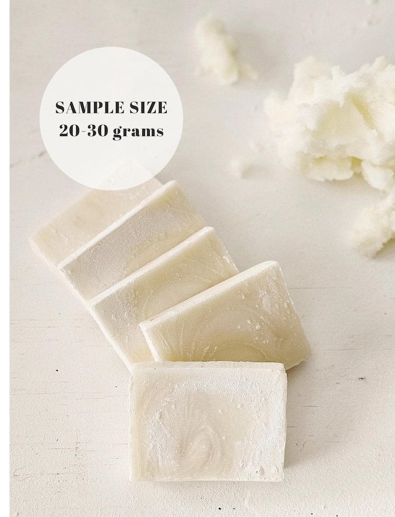 May include: A close-up of several rectangular bars of soap, arranged diagonally on a white surface. The soap is a creamy white color with a subtle marbled texture. The text "SAMPLE SIZE 20-30 grams" is in a white circle.