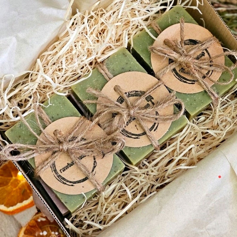 K&ouml;nnte beinhalten: Vier gr&uuml;ne Seifenst&uuml;cke, die mit Schnur und braunem Papier umwickelt sind, auf dem der Text "Rawhaus" steht. Die Seife befindet sich in einer Schachtel mit zerkleinertem Papier.