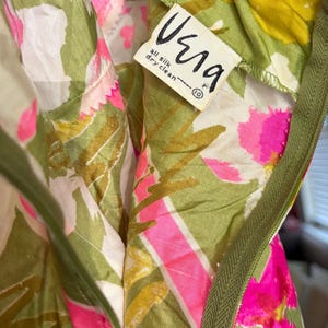 May include: A close-up of a vintage floral dress with a green zip and a "Vera" label. The dress has a bright pattern of pink, yellow, and green flowers on white. The label states the dress is all silk and dry clean only.