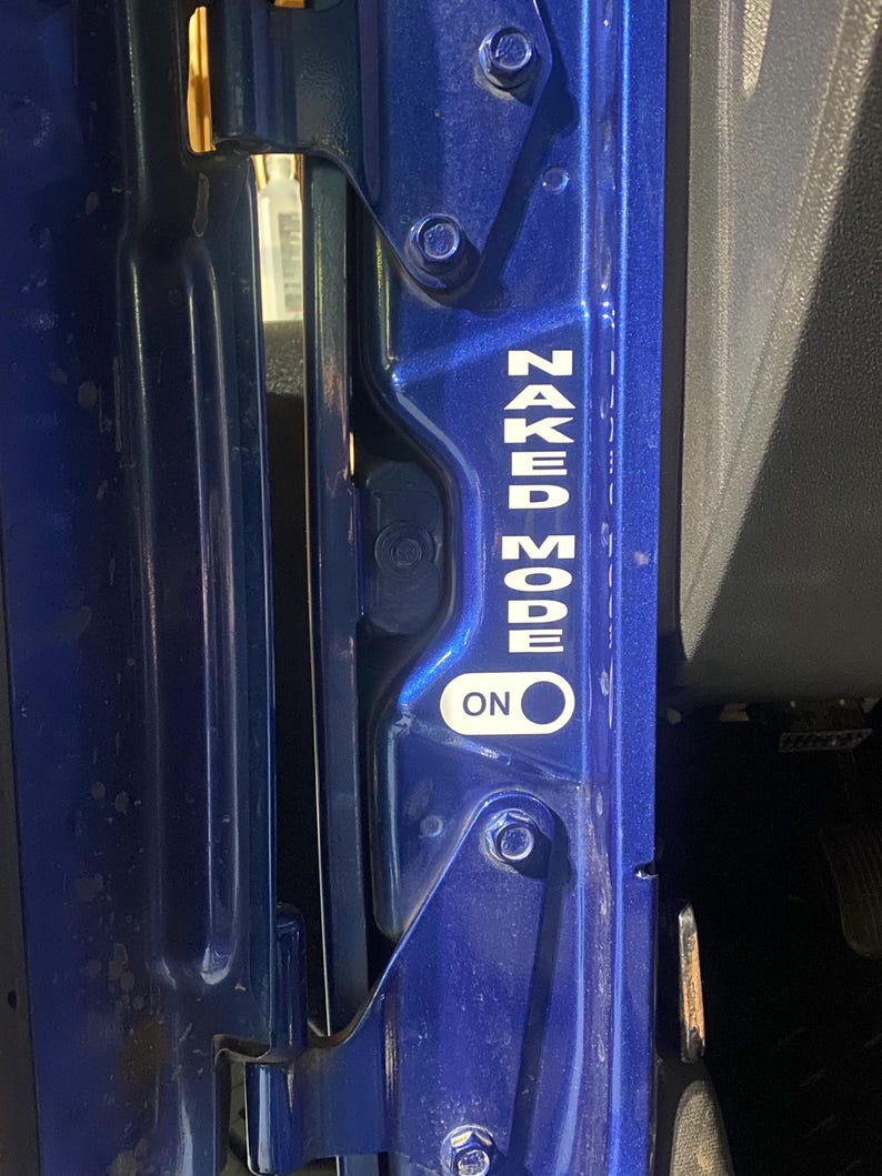 May include: Close-up of a blue vehicle door frame with the text "NAKED MODE ON" in white lettering. The door frame has visible hinges and bolts.