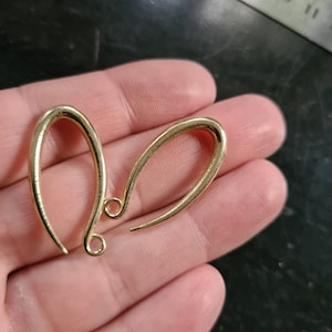 Könnte beinhalten: Zwei goldfarbene Ohrringhaken aus Metall. Die Haken sind tropfenförmig mit einer kleinen Schlaufe oben.