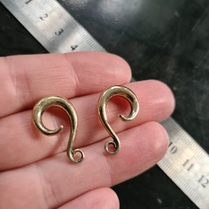Könnte beinhalten: Zwei goldfarbene Ohrdehner mit einem Spiraldesign. Die Dehnungen haben einen Durchmesser von etwa 2,5 cm.