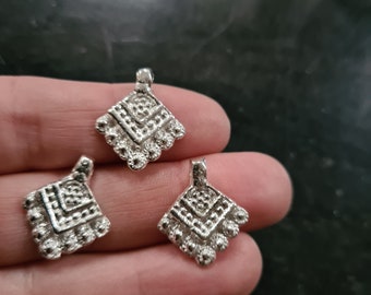 Könnte beinhalten: Drei silberne Anhänger mit geometrischem Design. Jeder Anhänger hat eine quadratische Form mit einem Diamantenmuster und einer abgerundeten Kante.