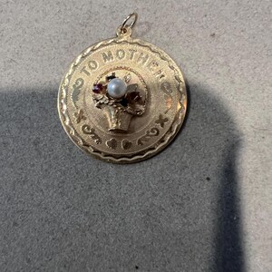 May include: Gold-toned pendant with a basket of flowers and a pearl in the center. The pendant is inscribed with the words "To Mother" and "Love You Always".