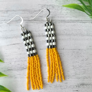 May include: A pair of dangle earrings with a black and white checkered pattern and a yellow fringe.