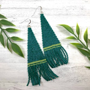 May include: A pair of long, green beaded earrings with a light green stripe. The earrings are hanging from silver hooks.