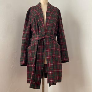 May include: A plaid robe in shades of burgundy, green, and white, displayed on a mannequin. The robe features a shawl collar, a waist tie, and two front pockets. The plaid pattern is a classic design.