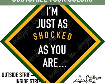 May include: A black diamond-shaped graduation cap with the text "I'm just as shocked as you are..." in white. The cap has a green outer border and a yellow inner border. The text "Outside Strip" and "Inside Strip" are labeled on the bottom left corner of the image.