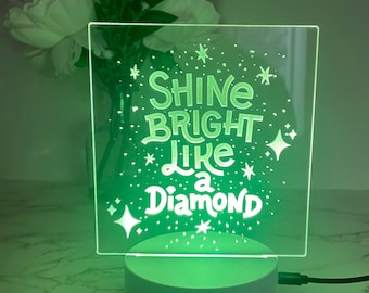 Pode incluir: Uma luz noturna LED verde com uma base branca. A luz apresenta o texto "Shine Bright Like a Diamond" com estrelas e brilhos ao redor do texto.
