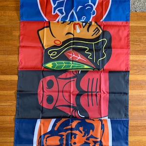 May include: A rectangular wall banner featuring four stacked sports team logos. The top section displays a blue bear logo, the second shows a black and red Native American profile, the third features a red bull head, and the bottom shows an orange bear.