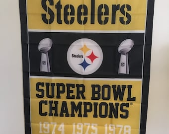 May include: A yellow and black NFL Pittsburgh Steelers Super Bowl Champions flag with the team logo and the years they won: 1974, 1975, 1978, 1979, 2005, and 2008.