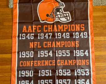 May include: A brown and orange NFL Cleveland Browns flag with a white helmet graphic and the text "Cleveland Browns", "AAFC Champions", "NFL Champions", "Conference Champions", and the years of each championship.