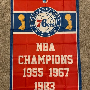 May include: A red and blue flag with the Philadelphia 76ers logo and the text "NBA CHAMPIONS 1955 1967 1983".