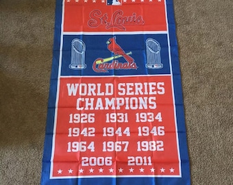 May include: A red and blue flag with the St. Louis Cardinals logo and the text "World Series Champions" with the years they won the World Series.