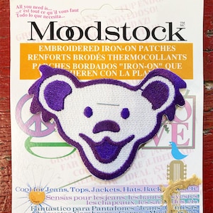 Peut inclure: Patch thermocollant brodé représentant un visage d'ours souriant en violet et blanc. Le patch est intitulé "Modstock" et indique "Renforts brodés thermocollants".