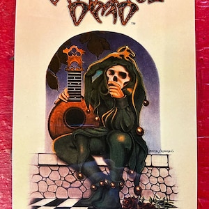 May include: A vintage Grateful Dead sticker featuring a jester-like figure with a skull face, holding a lute. The jester is dressed in green with gold accents, seated on a checkered floor. The Grateful Dead logo is at the top.