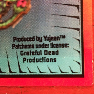 May include: Close-up of a blue and green fabric patch with black text that reads "Produced by Yujean&trade; Patches under license: Grateful Dead Productions".