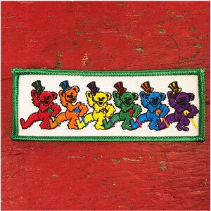 Puede incluir: Una fila de seis osos danzantes de colores que llevan sombreros de copa. Los osos son rojo, naranja, amarillo, verde, azul y morado.