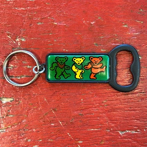 May include: A black bottle opener keychain with a green, yellow, and orange dancing bear design. The keychain has a silver key ring.