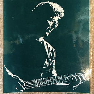 May include: A white silhouette of a person playing a guitar against a dark green background. The image is a stencil design.