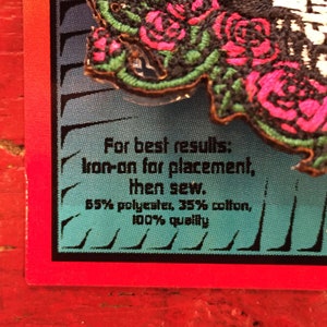 May include: Close-up of a black and green embroidered patch with pink roses. The patch has instructions for iron-on placement and sewing. The text reads: "For best results: Iron-on for placement, then sew. 55% polyester, 35% cotton, 100% quality"