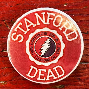 May include: A circular red button with white text reading "STANFORD DEAD". The centre has a circular design with a lightning bolt and the text "FROST AMPHITHEATRE AUG 20 21 1983 STANFORD CAL".