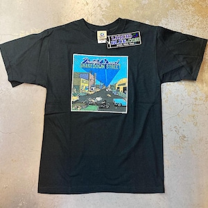 Könnte beinhalten: Schwarzes T-Shirt mit einer Grafik, die eine Straßenszene und den Text "Grateful Dead Shakedown Street" zeigt. Die Grafik ist mit blauem Himmel und Gebäuden umrahmt. Ein Liquid Blue-Etikett ist angebracht.