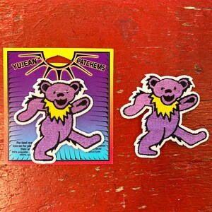May include: Purple iron-on patch of a dancing bear with a yellow collar. The patch is on a card with the text "YUJEAN PATCHEMS" and instructions for use.