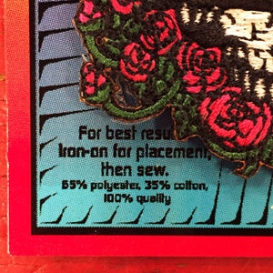 May include: A close-up of a black and white embroidered patch with red roses. The patch has instructions for best results: "Iron-on for placement, then sew. 65% polyester, 35% cotton, 100% quality."