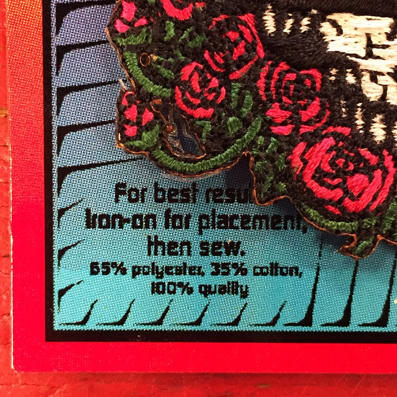 May include: A close-up of a black and white embroidered patch with red roses. The patch has instructions for best results: "Iron-on for placement, then sew. 65% polyester, 35% cotton, 100% quality."