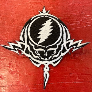 Peut inclure: Patch brodé blanc avec un crâne noir et des éclairs. Le crâne a un cercle noir avec un éclair blanc à l'intérieur.