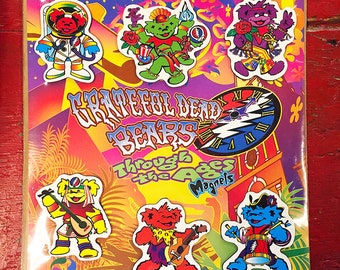 May include: A set of eight Grateful Dead Bears Through the Ages magnets. The magnets feature different bears in various poses and outfits, including a bear in a space suit, a bear playing a guitar, and a bear wearing a pirate hat. The magnets are colorful and feature a psychedelic design.
