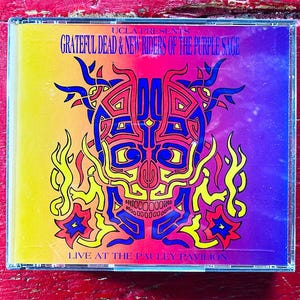 May include: A CD case featuring a vibrant, psychedelic design. The cover displays a skull with intricate patterns in red, blue, and yellow, surrounded by flames and stars. Text includes "UCLA PRESENTS GRATEFUL DEAD & NEW RIDERS OF THE PURPLE SAGE" and "LIVE AT THE PAULEY PAVILION."