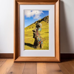 May include: A framed photograph of a large stone statue on Easter Island, covered in colorful graffiti, including the word "LOVE". The statue is standing in a grassy field with a blue sky and white clouds in the background.