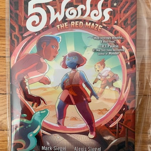 May include: A graphic novel cover with the title "5 Worlds: The Red Maze" in white text. The cover features three characters in a colorful, futuristic setting. The characters are a blue-skinned girl with red hair, a brown-skinned girl with short black hair, and a boy with brown hair. The cover also features a quote from R.J. Palacio, the author of "Wonder".