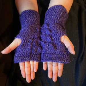 May include: A pair of purple fingerless gloves with a sparkly texture. The gloves are crocheted and have a finger hole on each glove.