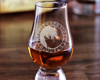 May include: A clear glass whisky tumbler with a design of two wolves and runes etched into the side. The glass is filled with amber liquid and is sitting on a wooden surface. The text "Geri & Freki" is at the top of the image.