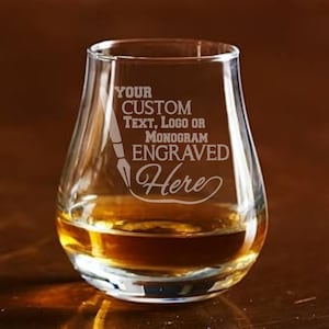 May include: A clear, stemless whiskey glass filled with amber liquid. The glass has a rounded base and a slightly flared top. Text on the glass reads "YOUR CUSTOM TEXT, LOGO OR MONOGRAM ENGRAVED Here".