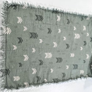 May include: A gray throw blanket with a white and black arrow pattern. The blanket has a frayed edge.