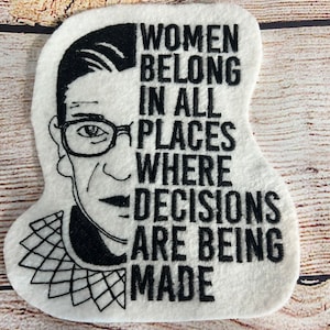 May include: Black and white embroidered patch featuring a portrait of Ruth Bader Ginsburg with the text "Women belong in all places where decisions are being made."