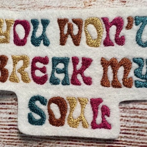 May include: Embroidered patch with the text "You won't break my soul" in a retro font. The letters are in different colors: gold, brown, teal, and pink.