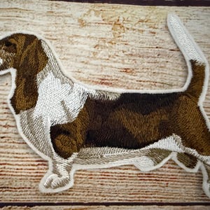 Könnte beinhalten: Gestickter Aufnäher eines braunen und weißen Basset Hundes auf weißem Hintergrund.